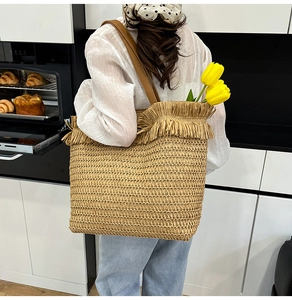 Detail of woven straw tote bag with fringe trim and leather straps in a home setting