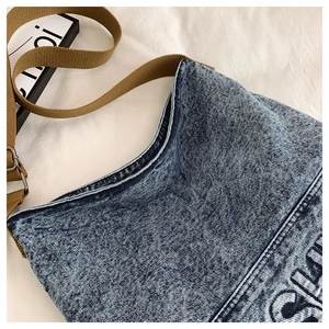 Detailed close-up of dark blue denim bag with embroidery and brown woven strap