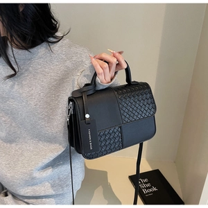 Detail of black faux leather handbag featuring a stylish checkered weave and top handle