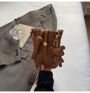 Detailed view of brown teddy bear crossbody phone bag with doll charm on white bedding