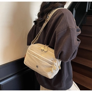 Détail latéral d'un sac bandoulière beige en nylon avec large sangle lettrée et multi-zips