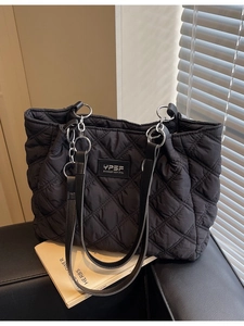Schwarze gesteppte Shopper-Tasche mit silberner Kette auf Ledersessel in moderner Umgebung