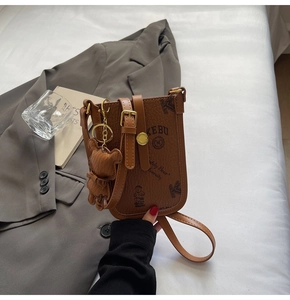 Brown leather mini crossbody bag with teddy bear print and charm in urban setting