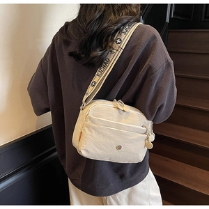 Détail du sac bandoulière en nylon crème avec plusieurs zips et sangle jacquard