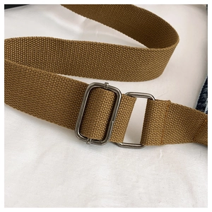 Detail of adjustable brown woven shoulder strap with matte metal hardware on denim bag