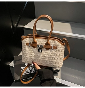 Detail of woven straw bag with leather trim and silver metal lock closure on gray stairs