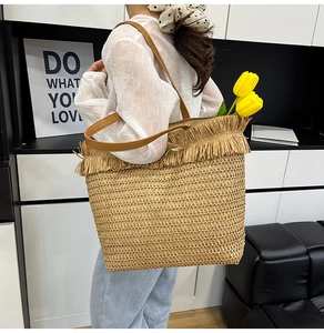 Detail of woven straw tote bag featuring stylish tassel trim and leather shoulder straps