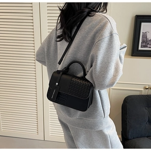 Detail of black crossbody bag featuring woven texture flap and fashion brand tag pendant
