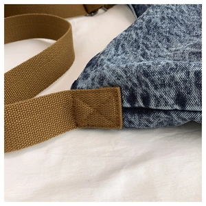 Detail of blue washed denim bag with brown reinforced canvas strap and X-shape stitching