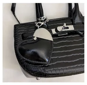 Close-up of black crocodile textured handbag with heart mirror charm and silver twist lock