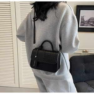 Detail of black woven leather crossbody bag with minimalist handle and fashion tag
