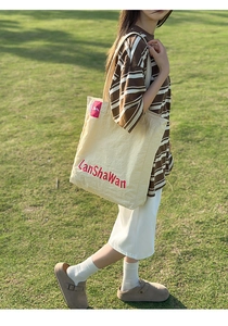 Détail du sac cabas en nylon crème avec broderie LanShaWan rouge sur herbe extérieure
