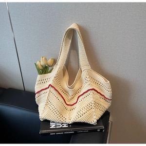 Detail of hand-woven hollow tote bag in beige with red wavy stitching on leather sofa
