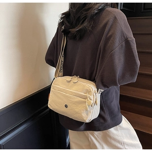 Détail du sac bandoulière en nylon beige avec zips multicouches et sangle jacquard
