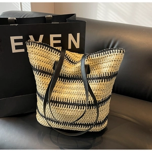 Détail du sac cabas en paille tressée à rayures noires et beige sur un canapé