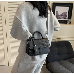 Close-up of black crossbody bag with woven texture detail and adjustable shoulder strap