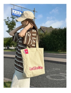 Photo street style d'un grand cabas en nylon beige avec broderie rouge et étiquette