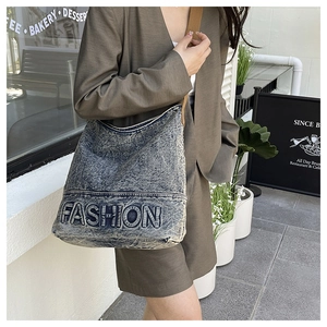 Close-up of blue denim tote bag with FASHION lettering and brown wide shoulder strap