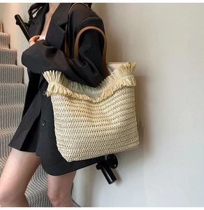 Detail of woven straw tote bag featuring long fringes and brown leather shoulder straps