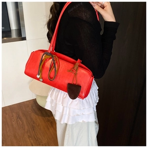 Détail du sac baguette rouge avec fermeture éclair nouée et breloques en forme de cœur
