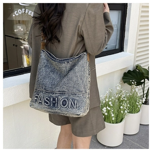 Detail of washed denim tote bag featuring blue FASHION embroidery and brown strap