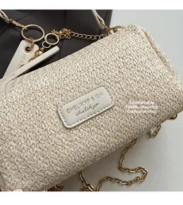 Detail of beige straw woven bag featuring a leather logo patch and golden chain strap