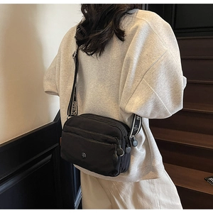 Détail du sac bandoulière en nylon noir multi-poches avec large sangle logotypée