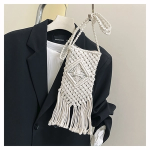Close-up of white woven cotton phone bag with boho tassels on black blazer