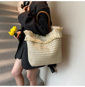 Detail of woven straw tote bag featuring decorative fringes and premium brown leather handles