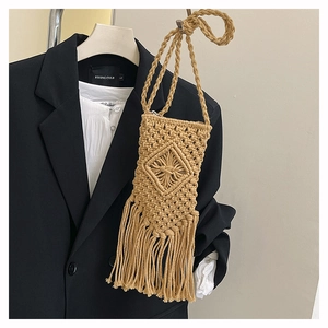 Detail of handmade macrame straw crossbody bag with long fringes on black suit