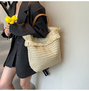 Close-up of woven straw tote bag featuring decorative fringe edge and brown leather straps