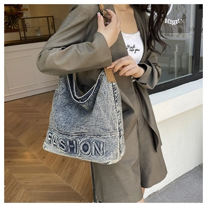 Detail of fashion denim tote bag with letter embroidery and brown woven straps