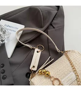 Detail of cream woven shoulder bag with gold chain strap and elegant brand tag decoration