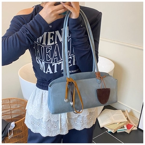 Détail du sac baguette en cuir bleu clair avec pendentif cœur argenté et pompons latéraux