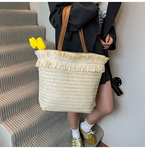 Detail of hand-woven straw tote with fringe trim and premium brown leather handles