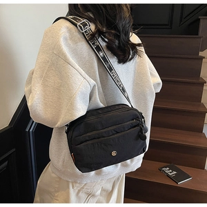 Détail du sac à bandoulière en nylon noir avec plusieurs zips et sangle à motifs mode