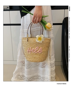 Detail der Strohhandtasche mit weißen Blumen und rosa Hello-Stickerei getragen vom Model