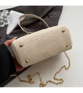 Detailed view of straw bag bottom with four protective gold metal feet and chain strap