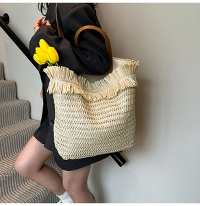 Detail of woven straw tote bag with fringe edge and brown leather shoulder straps