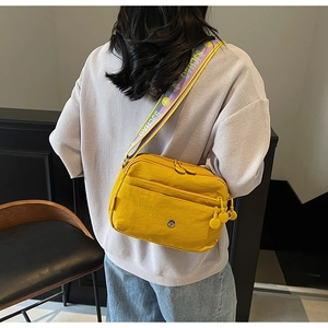 Détail du sac bandoulière en nylon jaune avec poches multiples et sangle lettrée
