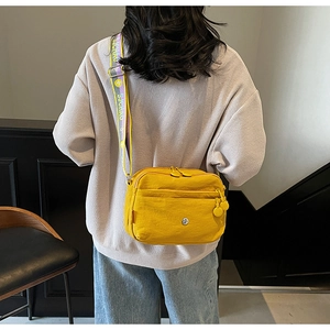 Détail du sac bandoulière en nylon jaune avec sangle large griffée et double zip