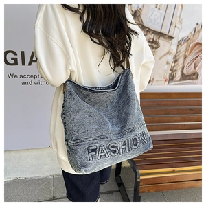 Side view of a large denim tote bag with FASHION embroidery worn on the shoulder