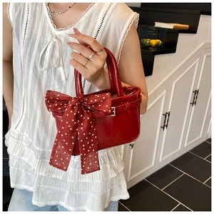 Detail of red glossy mini handbag featuring a large polka dot bow on white lace outfit