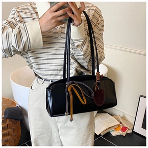 Détail d'un sac baguette noir brillant avec cordons tressés et breloques en forme de cœur