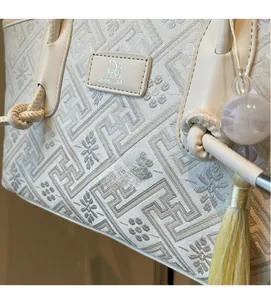 Detaillierte Nahaufnahme der beigen Jacquard-Stickerei und des Lederlogos der Handtasche