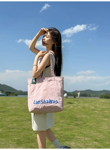 Détail du sac cabas en nylon rose avec texte bleu sur l'herbe ensoleillée