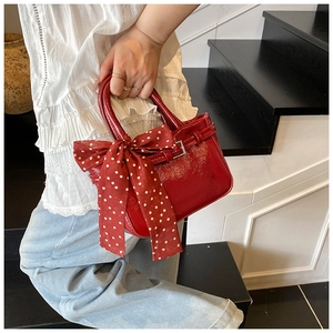 Detail of red patent leather handbag with decorative polka dot silk ribbon on handle