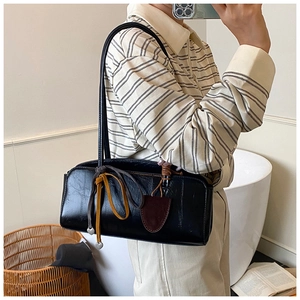 Détail du sac baguette noir brillant avec lanières décoratives et breloques en cœur