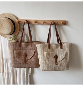 Detail of woven straw tote bags with leather straps and front pockets on wooden rack
