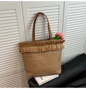 Detail of woven straw tote bag with decorative fringe and brown leather shoulder straps